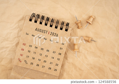 August 2026 desk calendar with wooden thumbtack on brown crumpled paper. 124588556