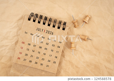 July 2026 desk calendar with wooden thumbtack on brown crumpled paper. July 2026 desk calendar with wooden thumbtack on brown crumpled paper. 124588578