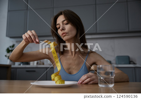 Skinny thin woman eating measuring tape demonstratively at home kitchen 124590136