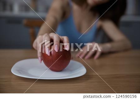 Sad woman taking an apple fruit on plate in home kitchen Sad woman taking an apple fruit on plate in home kitchen 124590156