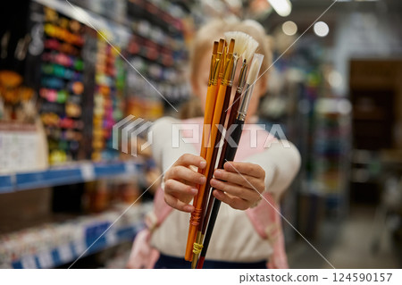 Cute little girl artist choosing new brush for painting in store Cute little girl artist choosing new brush for painting in store 124590157