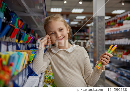 Portrait of happy satisfied schoolgirl choosing writing accessories for school 124590288