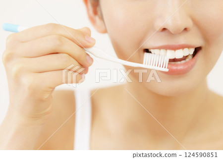 Close-up of the face under the eyes of a young woman brushing her teeth against a white background 124590851