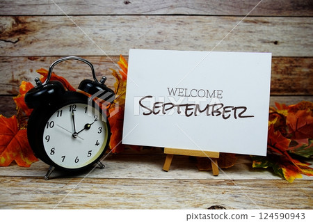 Welcome September text with alarm clock and maple leaf decoration on wooden background 124590943