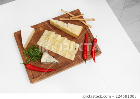 Cheese board on a white table. Different types of cheese, chili, microgreens, knife, bread sticks. Snack. 124591003