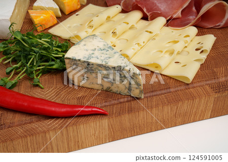 Cheese wooden board. Different types of cheese, chili, jamon, sausage, microgreens. Close up. Snack. Pieces of cheese. 124591005