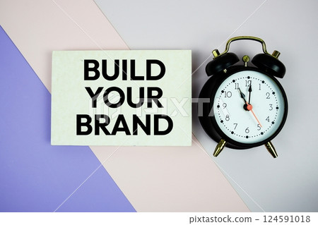 Build Your Brand text on paper card with alarm clock on purple and pink geometric background Build Your Brand text on paper card with alarm clock on purple and pink geometric background 124591018