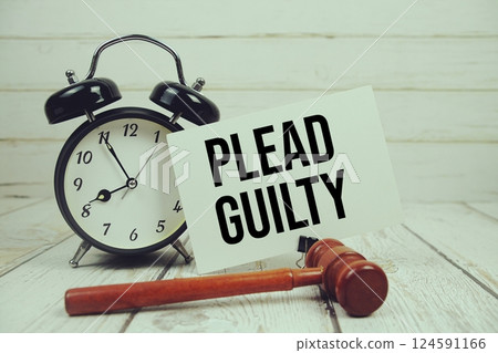 Plead Guilty text on paper card with alarm clock and wooden judge gavel on wooden background 124591166