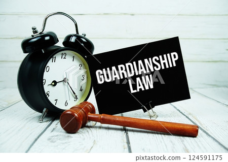 Guardianship Law text message on paper card with wooden gavel and alarm clock on green background Guardianship Law text message on paper card with wooden gavel and alarm clock on green background 124591175