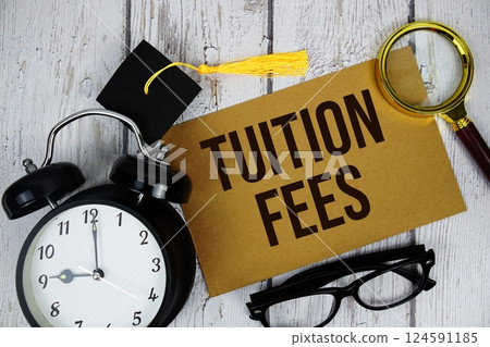Tuition fees text on paper card with alarm clock and magnifying glasstop view on wooden background Tuition fees text on paper card with alarm clock and magnifying glasstop view on wooden background 124591185