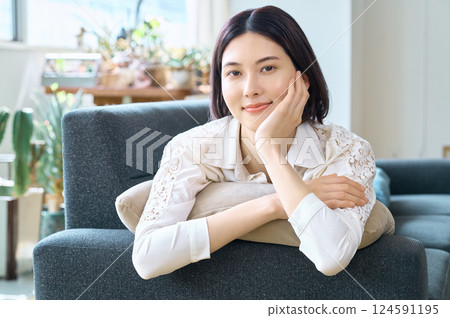 Smiling woman lying on sofa in living room 124591195