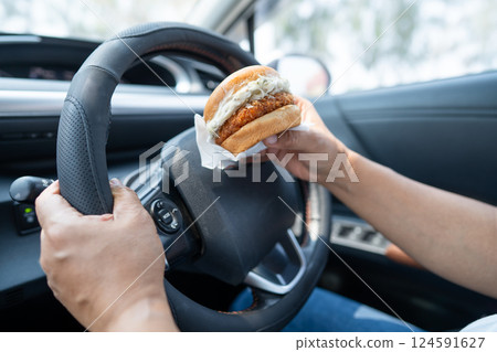 Asian lady holding hamburger to eat in car, dangerous and risk an accident. Asian lady holding hamburger to eat in car, dangerous and risk an accident. 124591627