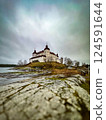 Fairytale Lacko Castle in autumn. View from the rocky shore of the lake. Gray cloudy sky above the castle.  124591644