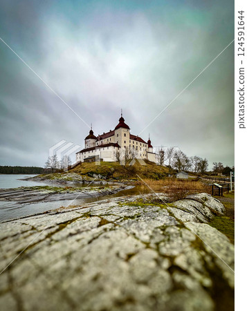 Fairytale Lacko Castle in autumn. View from the rocky shore of the lake. Gray cloudy sky above the castle.  124591644