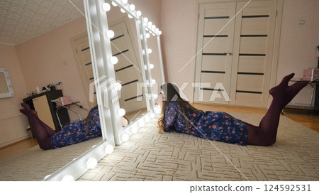 The girl is lying in front of the mirrors and flirting with herself. Manufacture of make-up mirrors. The girl is lying in front of the mirrors and flirting with herself. Manufacture of make-up mirrors. 124592531