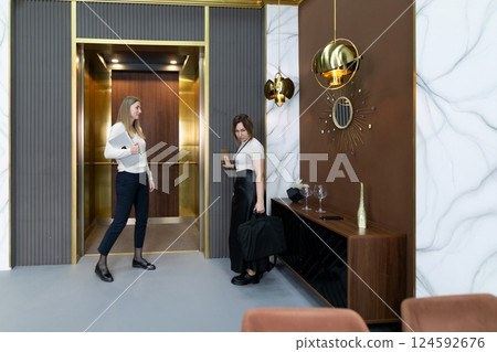 Two women in modern office lobby preparing for a meeting in a stylish elevator area 124592676