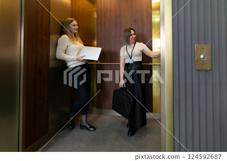 Professional women engage in conversation while waiting in an elevator during a busy workday at an 124592687