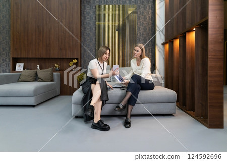 Two women engaged in discussion in a modern waiting area with stylish furnishings and warm lighting Two women engaged in discussion in a modern waiting area with stylish furnishings and warm lighting 124592696