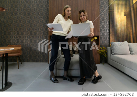 Two women reviewing documents in a modern living room during the afternoon Two women reviewing documents in a modern living room during the afternoon 124592708