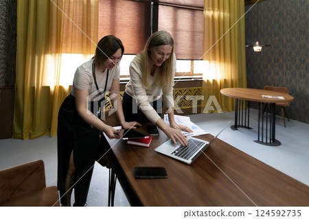 Two women collaborate on a laptop in a modern workspace during daytime while discussing their Two women collaborate on a laptop in a modern workspace during daytime while discussing their 124592735