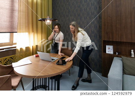 Two women discussing work tasks at a wooden table in a modern office during daylight hours Two women discussing work tasks at a wooden table in a modern office during daylight hours 124592979
