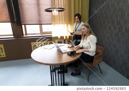 Two women working together in a cozy office space on a laptop while discussing ideas during the Two women working together in a cozy office space on a laptop while discussing ideas during the 124592983