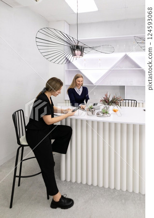Two women engaged in a conversation in a modern, minimalistic workspace during daylight hours 124593068