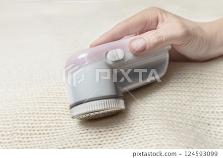 Machine for removing pellets from a woolen white jacket. A hand holds a reel removal machine close up photo Machine for removing pellets from a woolen white jacket. A hand holds a reel removal machine close up photo 124593099