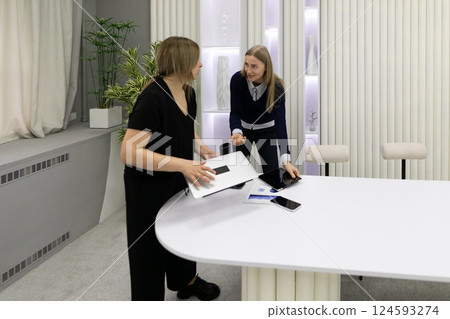 Two women discussing ideas while collaborating at a modern office table during daylight hours 124593274