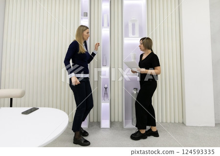 Two women engaged in conversation in a modern interior space during daylight hours Two women engaged in conversation in a modern interior space during daylight hours 124593335