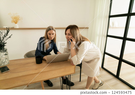 Two women collaborating on a project while discussing plans in a modern workspace during the day Two women collaborating on a project while discussing plans in a modern workspace during the day 124593475