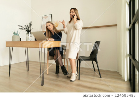 Two women engaged in conversation while working in a modern office space during the day 124593483