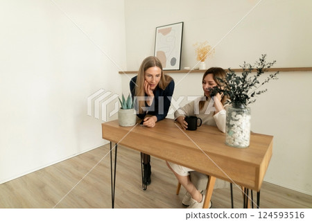 Two women discussing ideas at a minimalist wooden table in a bright, modern interior space during 124593516
