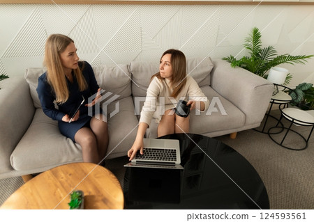 Two women engage in discussion while working on a laptop in a modern office space during the 124593561