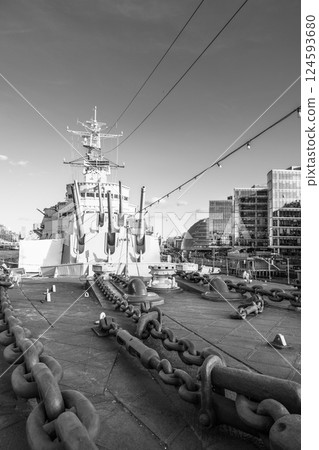 Turrets of HMS Belfast rise prominently, surrounded by historical architecture and modern buildings in London. The sun casts shadows, highlighting the ship's naval history and significance. Turrets of HMS Belfast rise prominently, surrounded by historical architecture and modern buildings in London. The sun casts shadows, highlighting the ship's naval history and significance. 124593680