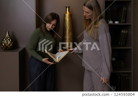 Two women discussing a book in a cozy interior setting during an afternoon gathering in a modern Two women discussing a book in a cozy interior setting during an afternoon gathering in a modern 124593804
