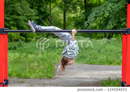 A fitness girl hangs upside down on a horizontal bar in a street gym. Outdoor fitness 124594033