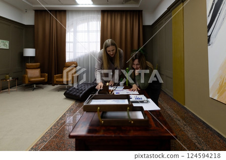 Two women collaborating on a project in a modern office setting with stylish furniture and artwork Two women collaborating on a project in a modern office setting with stylish furniture and artwork 124594218