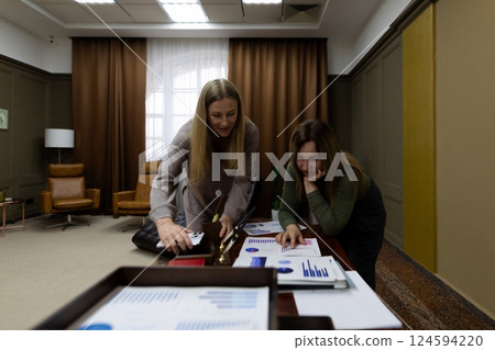 Two women collaborating on a business presentation in a modern office setting during the day 124594220