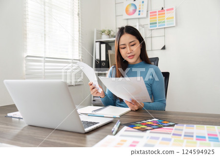 Design Review and Color Analysis. A creative professional examining design papers and color charts in a vibrant workspace. 124594925