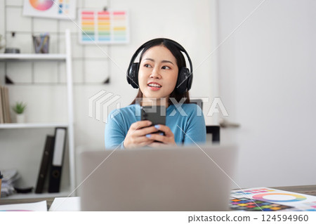 Engagement and Creativity. A graphic designer interacts with her smartphone while enjoying a coffee in a vibrant workspace. 124594960