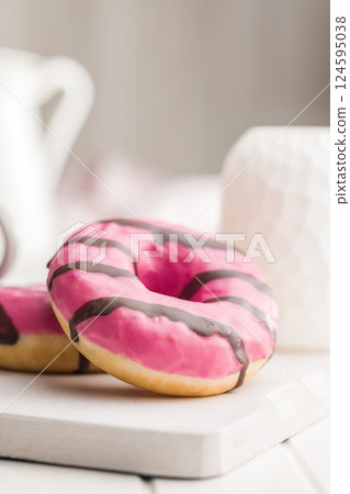 Sweet pink donut with chocolate strips on white table. Sweet pink donut with chocolate strips on white table. 124595038