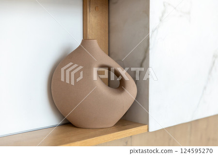 A modern matte curved shaped ceramic vase with an unusual wavy brown shape on the shelf. 124595270