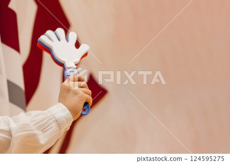 A fan's sports toy is a noisy hand with fingers in a woman's hand, red-white-blue on a beige background. 124595275