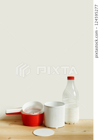 Plastic equipment for making soft cheese and cottage cheese at home. A white uniform, a red ladle and a bottle of milk. Copy space 124595277