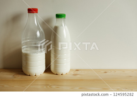 Two transparent plastic milk bottles on the table on a light monochrome background. 124595282