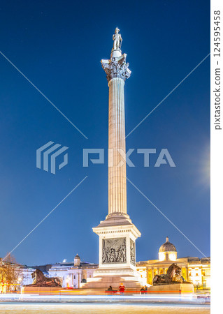 Nelson's Column stands tall in Trafalgar Square at night, surrounded by historical architecture and glowing under the city lights. The monument honors Vice-Admiral Horatio Nelson's victory. 124595458