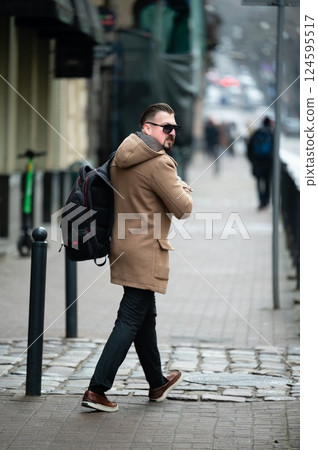 Urban winter stroll with fashion-forward style as a man navigates a bustling city street in a cozy coat, capturing the essence of cold-weather attire and city life 124595517