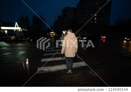 Walking across a dimly lit crosswalk during a rainy evening in a quiet urban neighborhood, with reflections glistening on the wet pavement 124595534