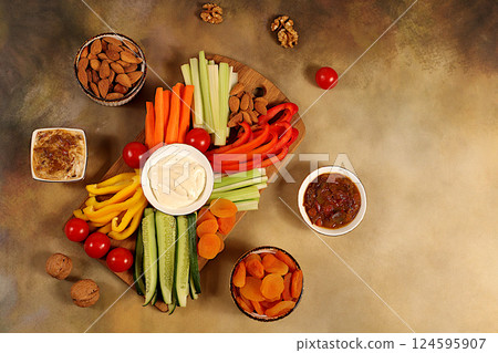 Middle East plate, Healthy food cuisine background with hummus bowl and raw vegetable sticks, nuts and dried apricots. Hummus platter with appetizers, traditional vegan snacks, oriental cuisine Middle East plate, Healthy food cuisine background with hummus bowl and raw vegetable sticks, nuts and dried apricots. Hummus platter with appetizers, traditional vegan snacks, oriental cuisine 124595907